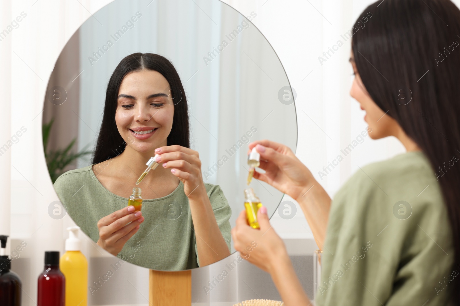 Photo of Beautiful woman holding bottle of serum in room. Cosmetic product