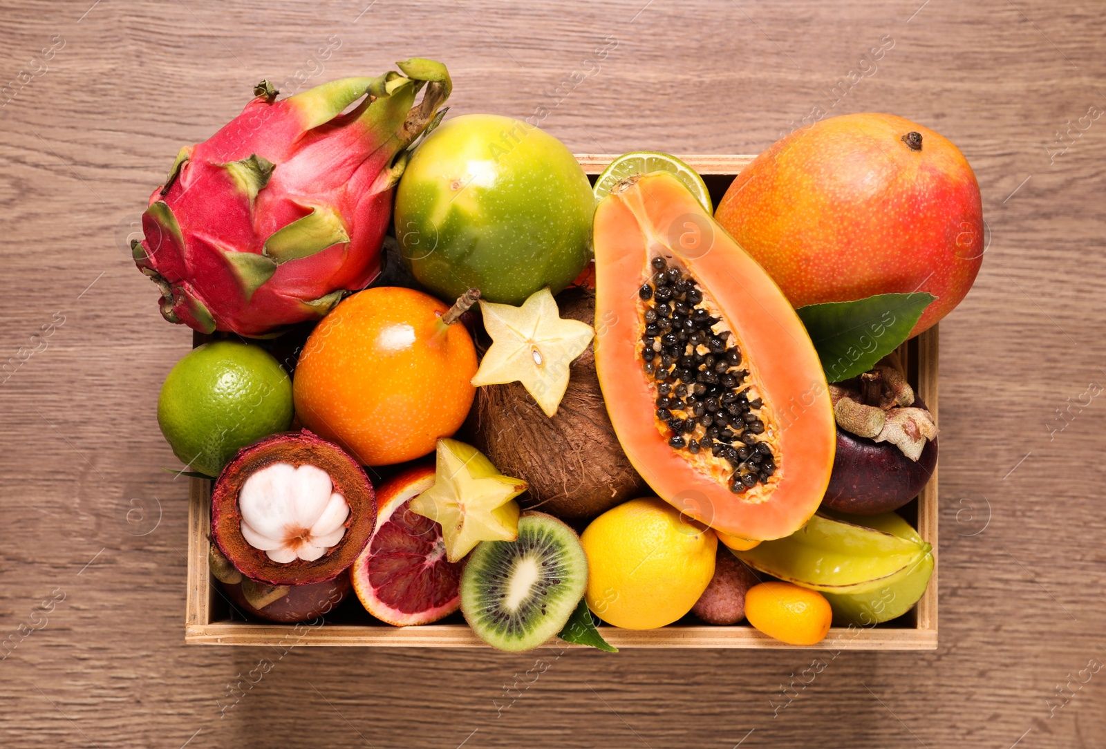 Photo of Different tropical fruits in box on wooden table, top view
