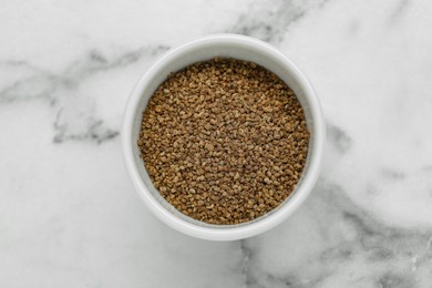 Bowl of celery seeds on white marble table, top view