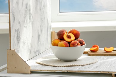 Photo of Bowl of juicy peaches and double-sided backdrop on table in photo studio