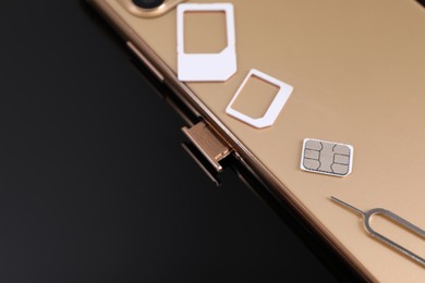 SIM card, smartphone and ejector on black background, closeup