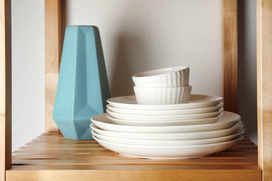Photo of Set of dinnerware on wooden shelf against light background. Interior element