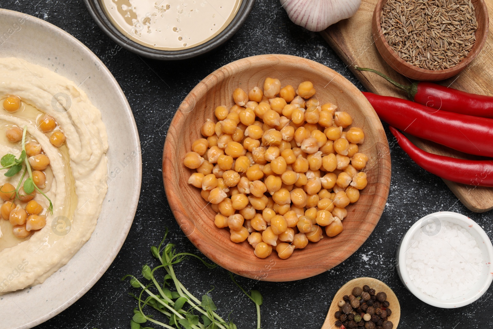 Photo of Delicious chickpeas and different products on black textured table, flat lay. Hummus ingredient