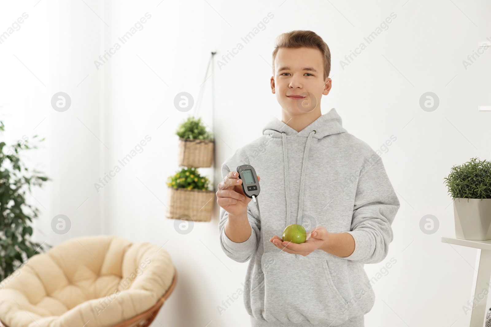 Photo of Teen boy holding digital glucometer and apple at home. Diabetes diet