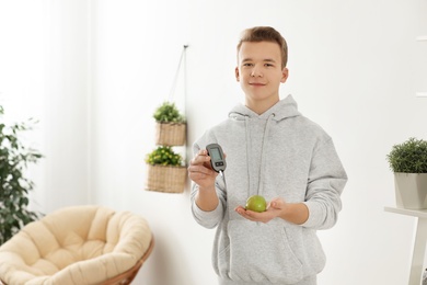 Photo of Teen boy holding digital glucometer and apple at home. Diabetes diet