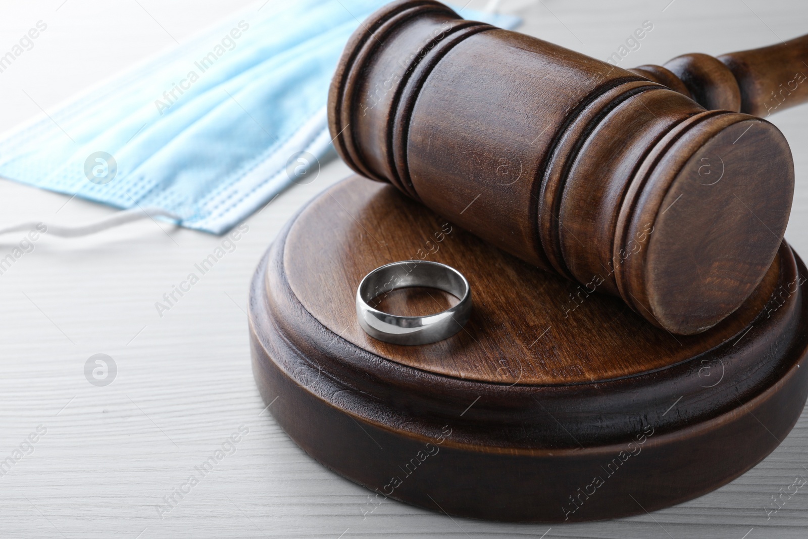 Photo of Gavel, wedding ring and protective mask on white wooden table. Divorce during coronavirus quarantine