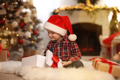 Cute little boy opening gift box in room decorated for Christmas