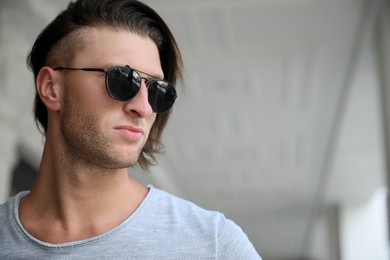 Photo of Portrait of handsome young man in stylish sunglasses indoors. Space for text