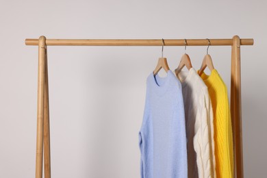 Photo of Rack with different warm sweaters on light background