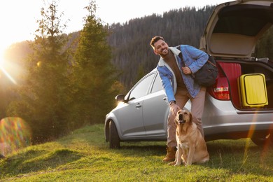 Happy man and adorable dog near car in mountains. Traveling with pet