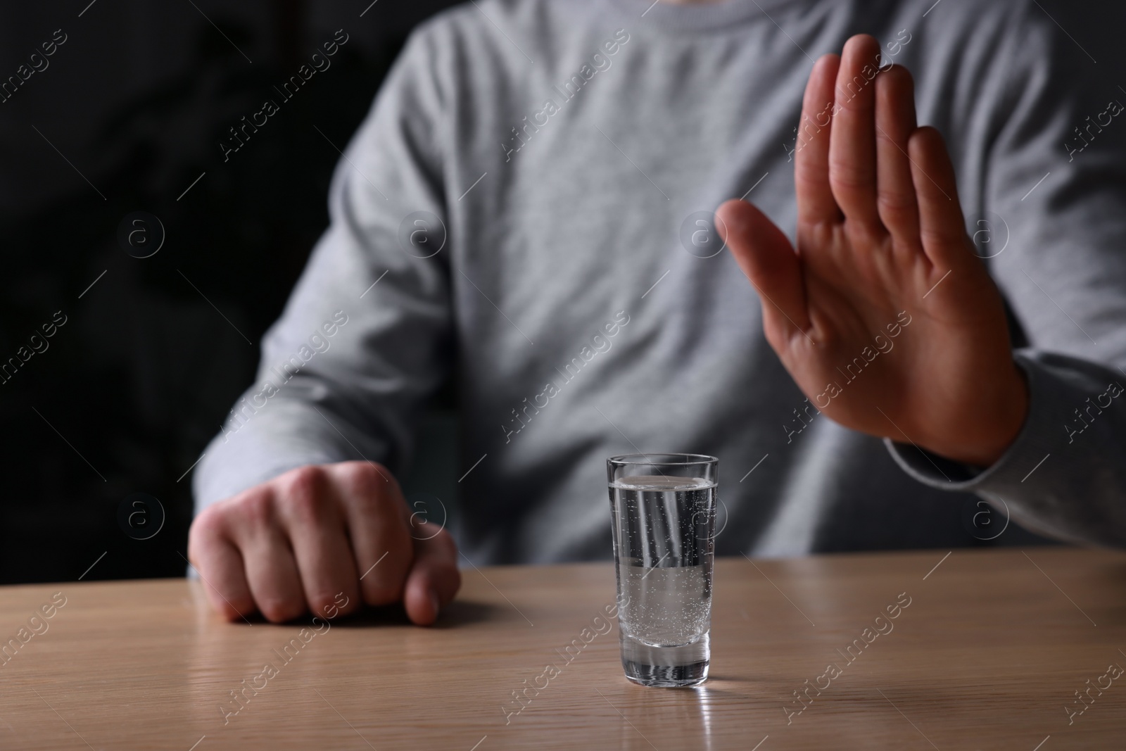 Photo of Man refusing to drink vodka at wooden table, closeup. Alcohol addiction