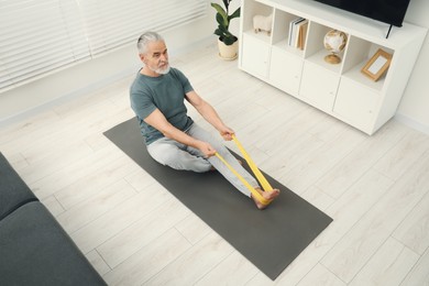 Senior man doing exercise with fitness elastic band on mat at home, above view