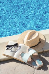 Photo of Stylish sunglasses, slippers, straw hat and book at poolside on sunny day. Beach accessories