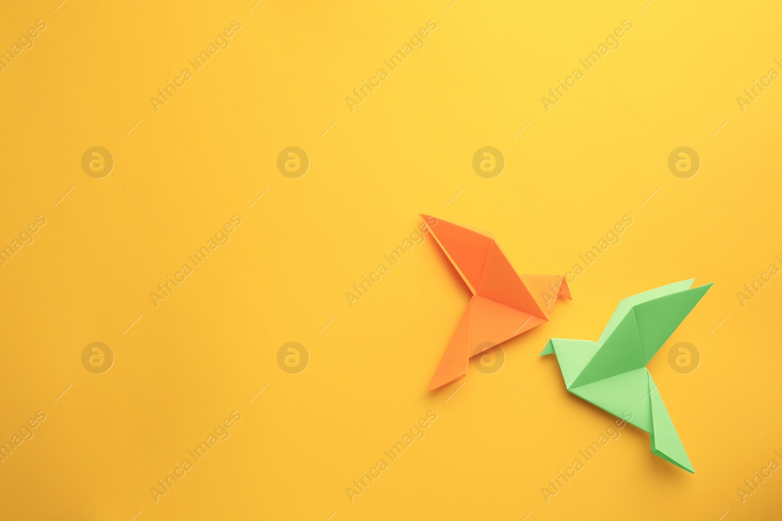 Photo of Origami art. Colorful handmade paper birds on yellow background, flat lay. Space for text