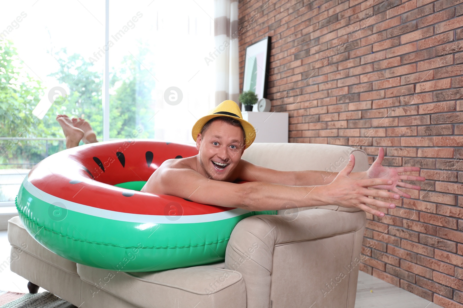 Photo of Shirtless man having fun with inflatable ring on sofa at home