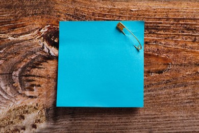 Photo of Light blue paper note attached with safety pin on wooden table, top view. Space for text