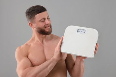 Athletic man holding scales on grey background. Weight loss concept