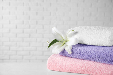 Photo of Stack of clean bath towels and beautiful flower on white wooden table. Space for text