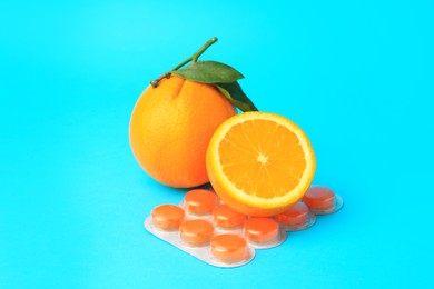 Photo of Blisters with cough drops and fresh oranges on light blue background