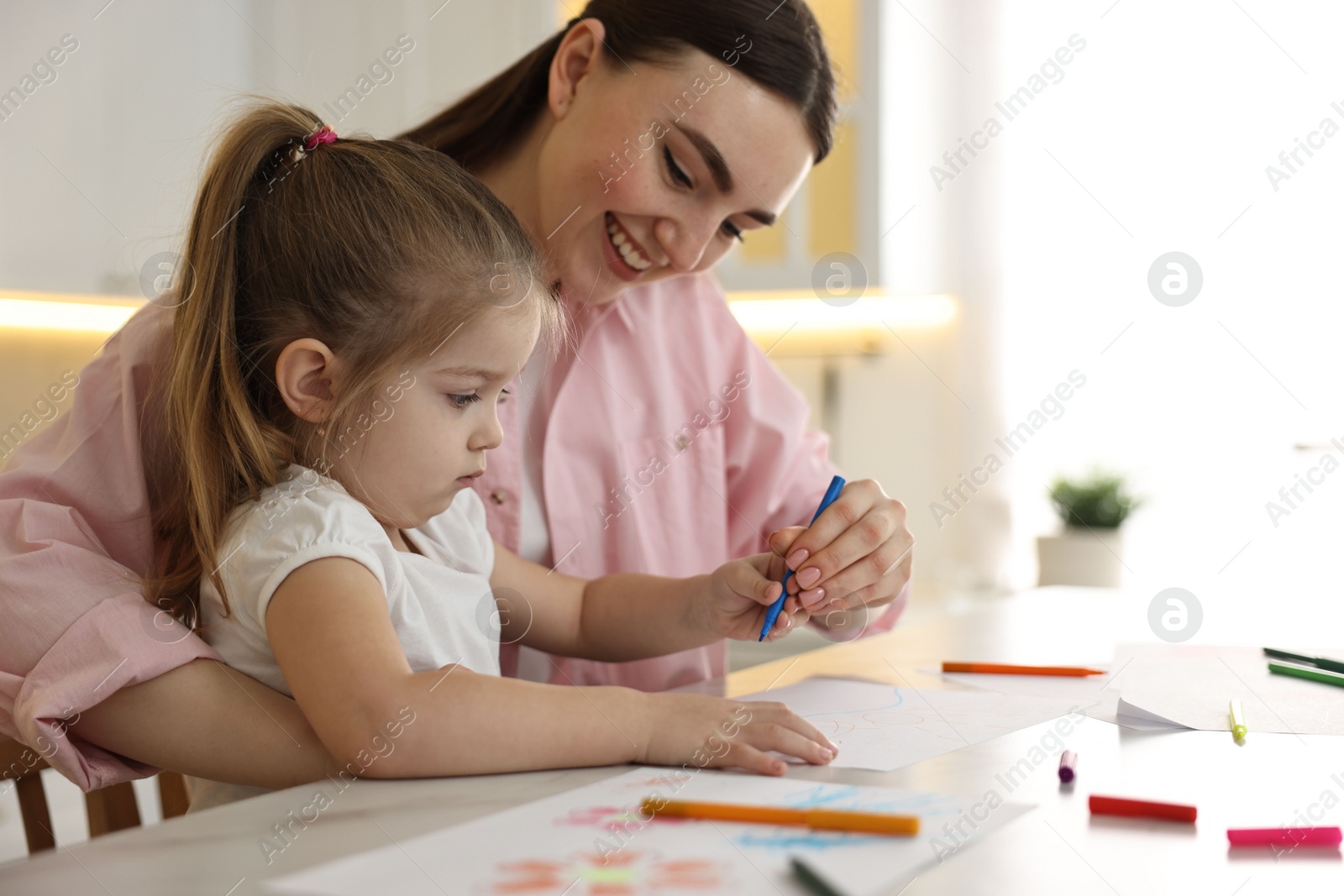 Photo of Mother and her little daughter drawing with colorful markers at table in kitchen