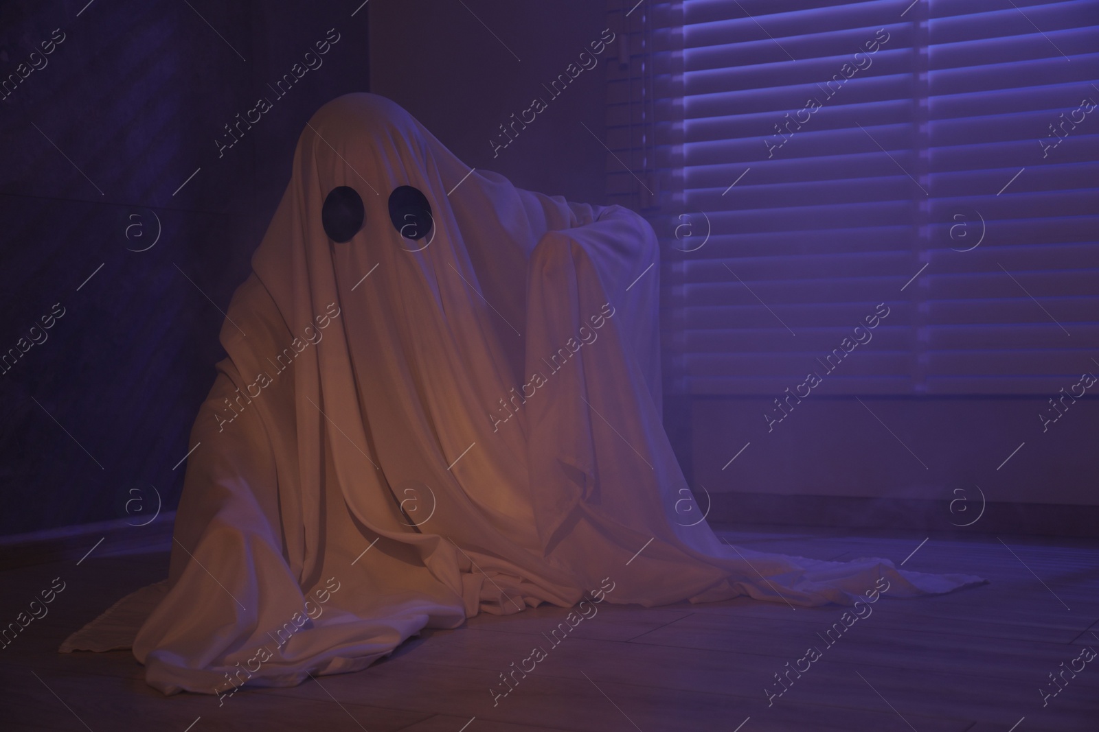 Photo of Creepy ghost. Woman covered with sheet near window in color lights, space for text