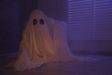 Photo of Creepy ghost. Woman covered with sheet near window in color lights, space for text