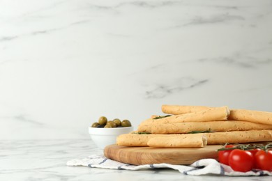 Photo of Tasty grissini with rosemary, tomatoes and olives on white marble table, space for text