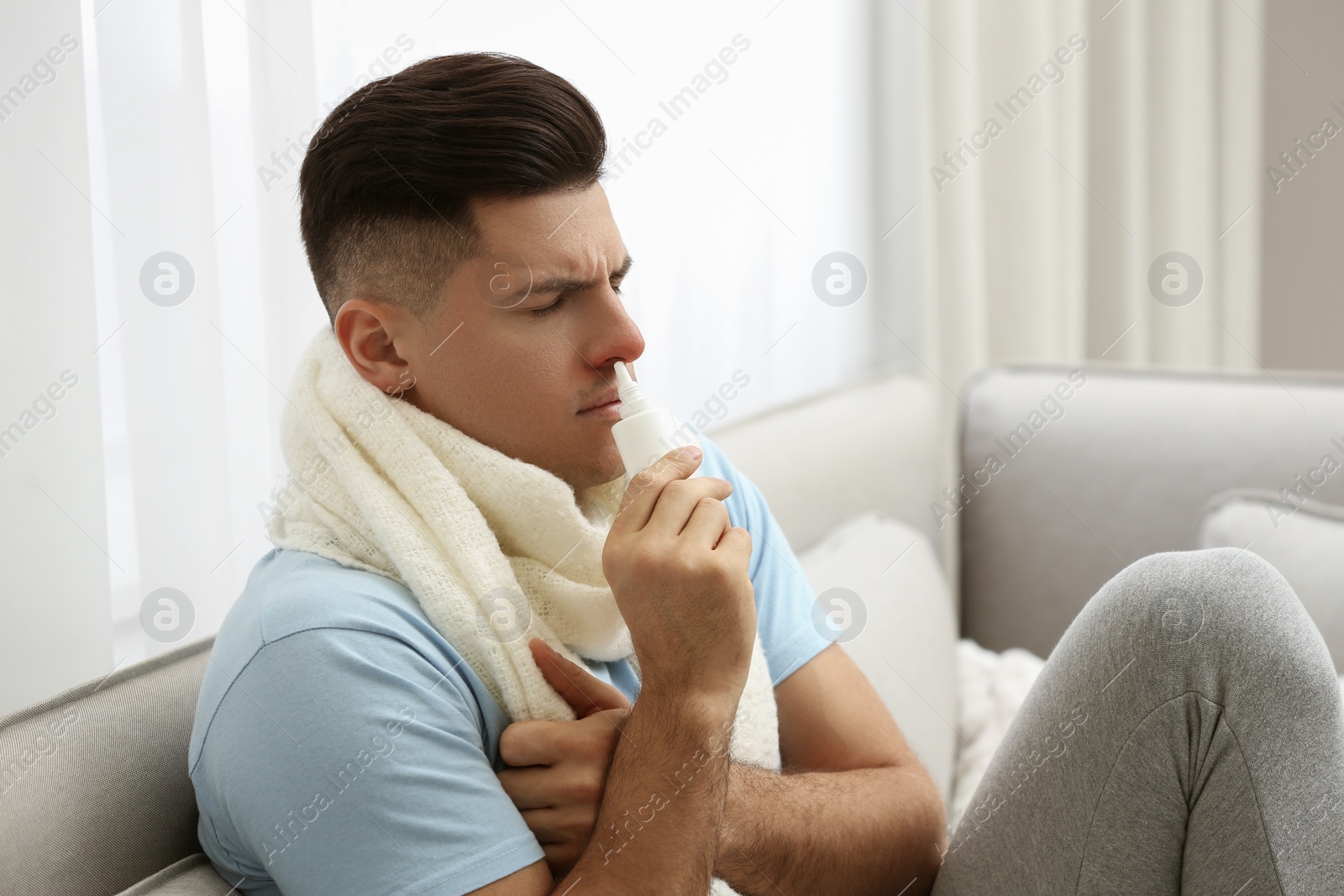 Photo of Ill man using nasal spray on sofa at home