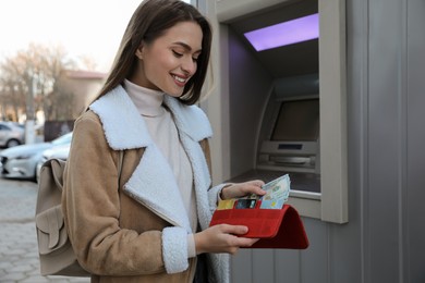 Photo of Woman putting money into wallet near cash machine outdoors