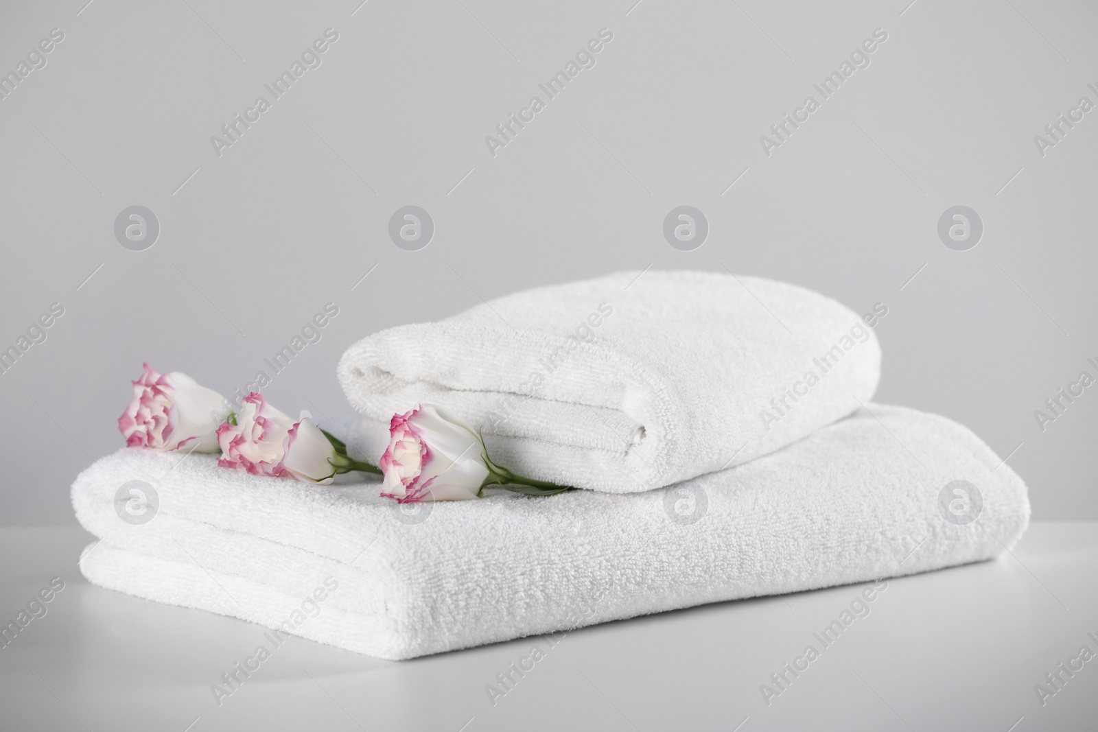 Photo of Folded soft towels with flowers on white table