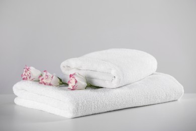 Folded soft towels with flowers on white table