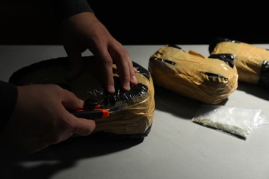 Photo of Smuggling and drug trafficking. Man opening package of narcotics with box cutter at light table against black background, closeup