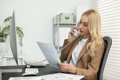 Secretary with document talking on smartphone at table in office