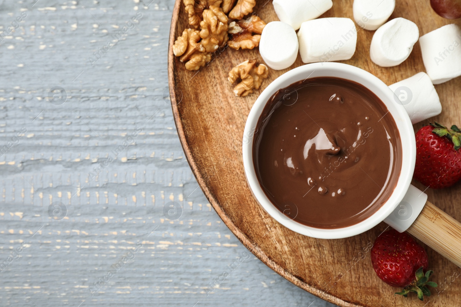 Photo of Fondue pot with milk chocolate and products on grey wooden table, top view. Space for text