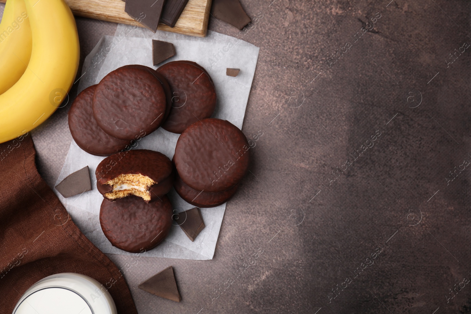 Photo of Tasty banana choco pies, pieces of chocolate and fruits on textured table, flat lay. Space for text