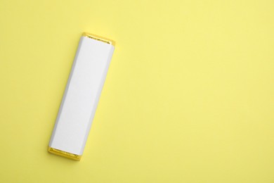 Tasty chocolate bar in package on light yellow background, top view. Space for text