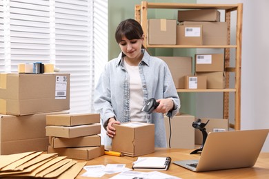 Photo of Parcel packing. Post office worker with scanner reading barcode at wooden table indoors