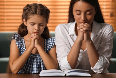 Photo of Young woman with her little daughter praying together over Bible at home