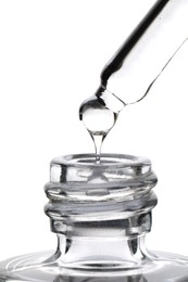Dripping clear facial serum from pipette into glass bottle on white background, closeup