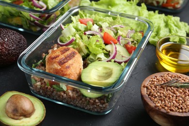 Photo of Healthy meal. Fresh salad, avocado, cutlet and buckwheat in glass container near other products on black table, closeup