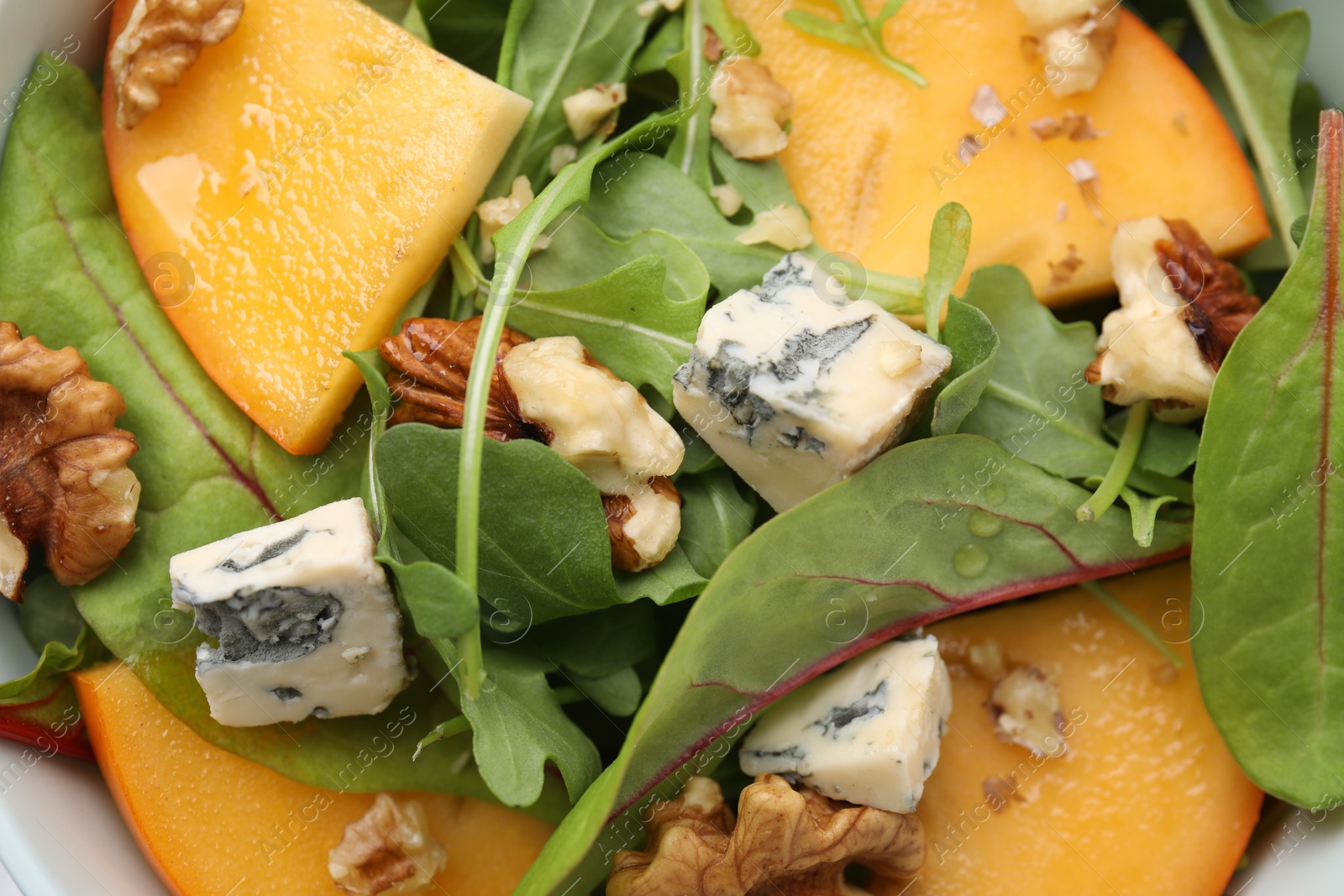 Photo of Tasty salad with persimmon, blue cheese and walnuts as background, top view