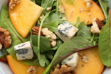 Tasty salad with persimmon, blue cheese and walnuts as background, top view