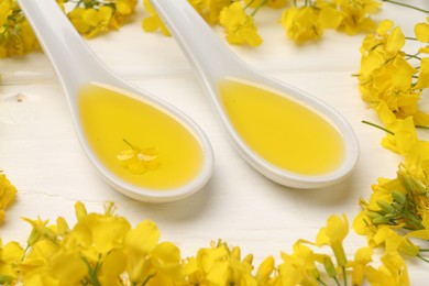 Photo of Rapeseed oil in gravy boats and beautiful yellow flowers on white wooden table, closeup