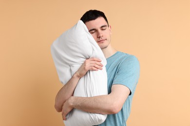 Photo of Man in pyjama holding pillow and sleeping on beige background