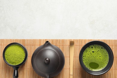 Photo of Cup of fresh matcha tea, teapot, spoon and green powder on light grey table, top view. Space for text