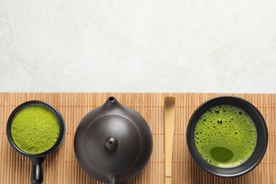 Cup of fresh matcha tea, teapot, spoon and green powder on light grey table, top view. Space for text