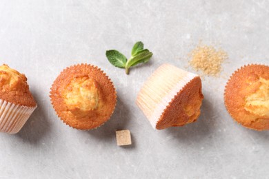 Photo of Delicious sweet muffins and brown sugar on light grey textured table, flat lay