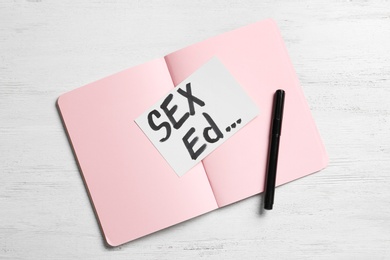 Photo of Notebook with text "SEX ED..." on white wooden background, top view