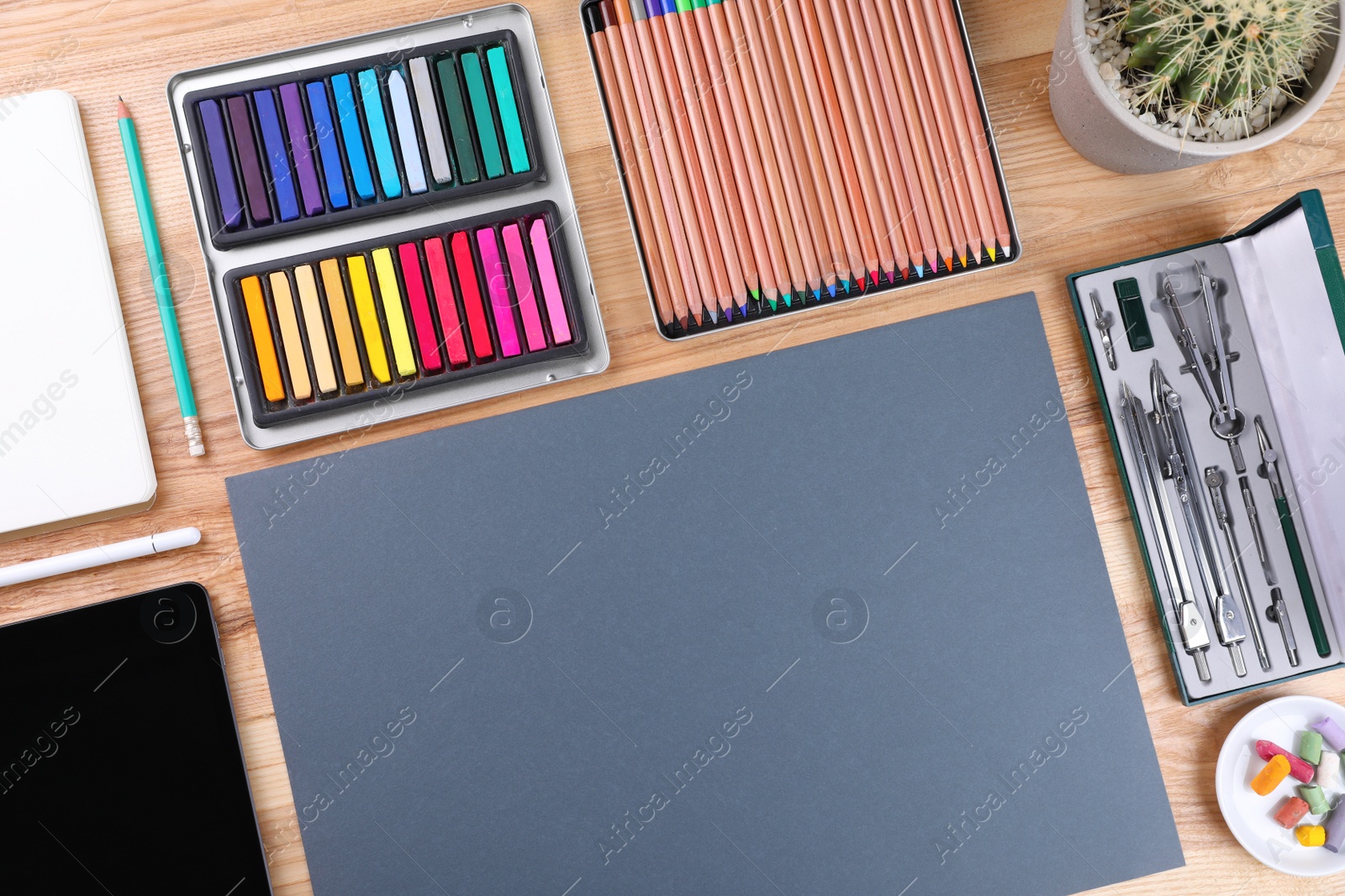 Photo of Layout with blank paper, soft pastels and other drawing supplies on wooden table at artist's workplace, top view. Space for design