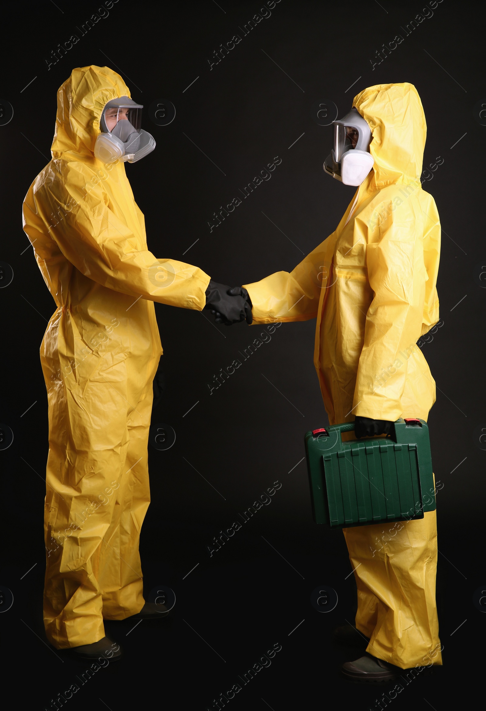 Photo of Man and woman in chemical protective suits shaking hands on black background. Virus research